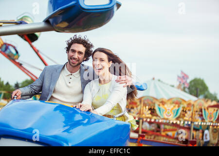 Couple enjoying ride sur carrousel en amusement park Banque D'Images