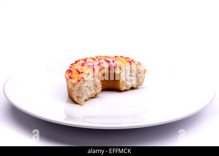 Bague donut glacé à moitié mangé sur une plaque sur un fond blanc. Banque D'Images