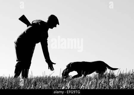 Garde-chasse avec chien dans le champ de la récupération d'oiseaux, silhouette noir et blanc Banque D'Images