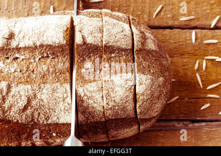 Pain de seigle de coupe avec un couteau sur une planche en bois Banque D'Images