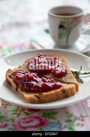 Plaque blanche avec des toasts et de la confiture avec cuvette sur nappe rose avec des fleurs Banque D'Images