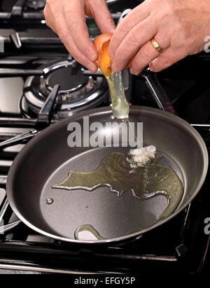 Une femme la fissuration ouvrir un oeuf dans une poêle sur une cuisinière à gaz Banque D'Images