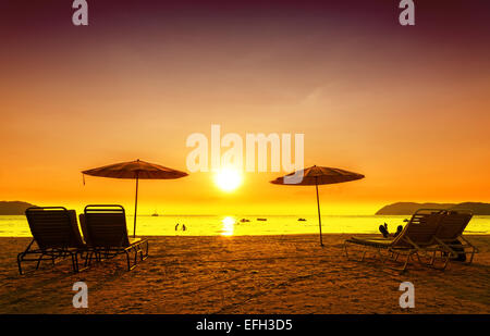 Retro photo filtrée de chaises de plage et parasols sur le sable au coucher du soleil. Concept pour le repos, détente, vacances. Banque D'Images