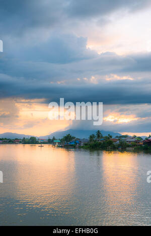 Nuages au coucher du soleil sur la rivière Sarawak à partir de la promenade du bord de mer de Kuching, Malaisie, Bornéo. Vue d'un village sur pilotis. Banque D'Images