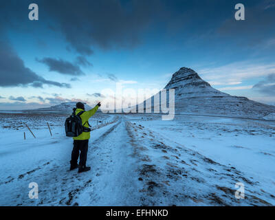 Un photographe solitaire dans une veste vert lime, transportant un sac à dos sur son dos prend dans la vue panoramique Vista à Kirkjufellsa Banque D'Images