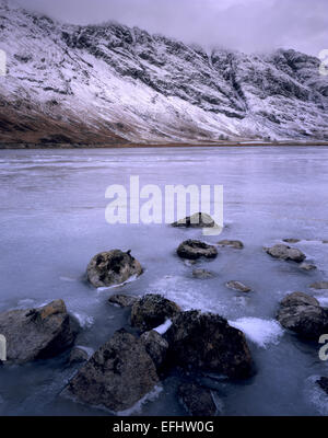 Surface gelée du Loch en Achtriochtan Glencoe avec l'Aonach Eagach couvertes de neige au-delà de la crête, Lochaber, Highlands écossais Banque D'Images