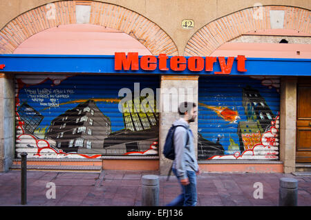 Un homme qui marche sur un graffiti urbain passé avant la boutique, Rue de Rome, Toulouse, Haute-Garonne, France Banque D'Images