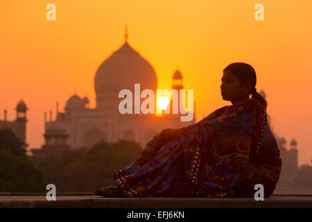 L'Inde, Uttar Pradesh, Agra, jeune femme indienne dans l'humeur contemplative au coucher du soleil avec Taj Mahal à distance Banque D'Images