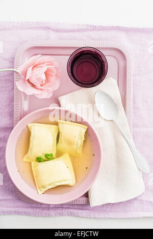 Maultaschen pâtes carrés dans un bouillon avec de l'eau et une fleur en papier crêpe sur un plateau Banque D'Images