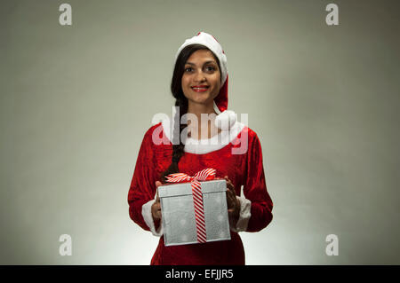 Jeune femme latine wearing Santa hat holding gift Banque D'Images