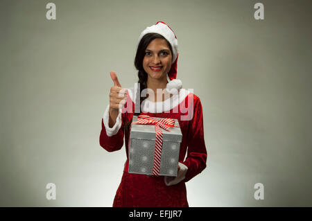 Jeune femme latine wearing Santa hat holding gift Banque D'Images