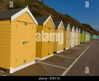L'or et crème des cabines de plage avec les portes bleues et rouges dans une ligne de structure et un abri traditionnel anglais trouvés au bord de la mer Banque D'Images