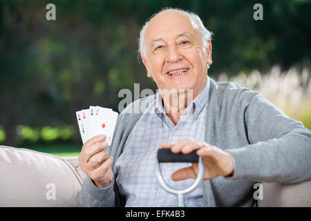 Senior man holding quatre as while sitting on couch Banque D'Images