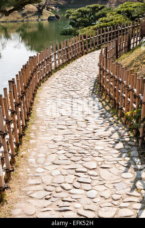 Jardin de Ritsurin-koen, Takamatsu, Japon. Un chemin traditionnel fait de pavés et bordé de clôtures basses en bambou Banque D'Images