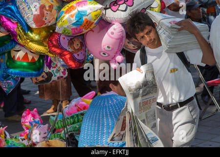 Oaxaca, Mexique - un homme à vendre des journaux dans le Zócalo (place centrale) passe devant une femme vendant des ballons. Banque D'Images