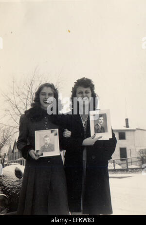 Le Canada. Dec 12, 2014. CIRCA 1950 : Reproduction d'une photo montre deux jeune fille dans un manteau posant sur un fond de la chambre avec des photos de militaires, hommes © Igor Golovniov/ZUMA/ZUMAPRESS.com/Alamy fil Live News Banque D'Images