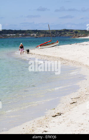 Femme et chien se promener au bord de l'eau sur une plage de sable, îles Scilly, uk Banque D'Images