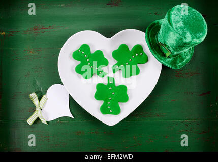 Happy St Patricks Day shamrock fondant vert forme des cookies sur la plaque en forme de coeur blanc sur vert style vintage table en bois. Banque D'Images