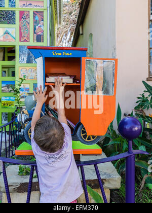 Un jeune garçon tient un livre qu'il vient d'une petite bibliothèque gratuite construit sous la forme d'une ancienne voiture. Banque D'Images