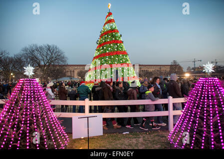 Arbre de Noël de la Maison Blanche Washington DC | WASHINGTON — Des foules se rassemblent au crépuscule autour de l’Arbre de Noël national sur l’Ellipse près de la Maison Blanche à Washington, D.C., ses lumières rouge et verte brillant sous un ciel d’hiver qui s’assombrit. Allumé pour la première fois en 1923 sous la présidence de Calvin Coolidge, l’arbre est le point central d’une tradition annuelle de vacances marquée chaque année par une cérémonie d’allumage présidentielle. Banque D'Images