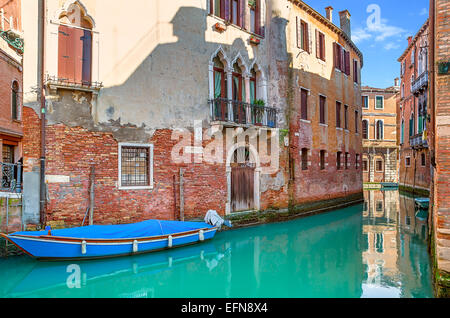 Bateau sur canal étroit entre les maisons anciennes en brique à Venise, Italie. Banque D'Images