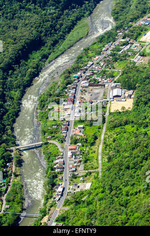 Une photographie aérienne montre une rivière sinueuse traversant une vallée verdoyante, flanquée de collines boisées denses. Le long de la rive, un petit village avec des maisons et des bâtiments dispersés est visible Banque D'Images
