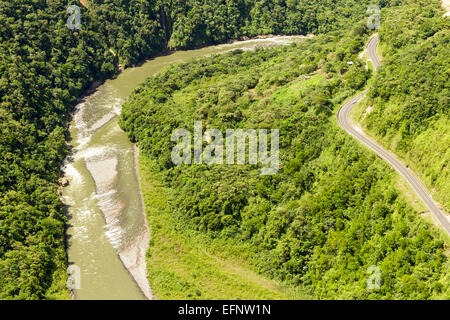 Une perspective aérienne montre une route sinueuse longeant une large rivière boueuse à travers un paysage boisé dense et verdoyant. La rivière serpente à travers la vallée, avec des bancs de sable visibles et peu profonds Banque D'Images