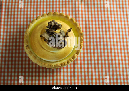 Gâteau au citron et meringue italienne, décoré avec des copeaux de chocolat sur la nappe à carreaux orange Banque D'Images