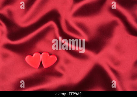 Le concept des deux amoureux coeur allongé sur le satin rouge, peut être utilisé comme arrière-plan, la texture Banque D'Images