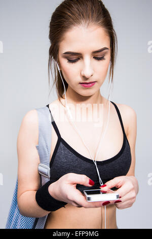 Sports woman using smartphone avec un casque sur fond gris Banque D'Images