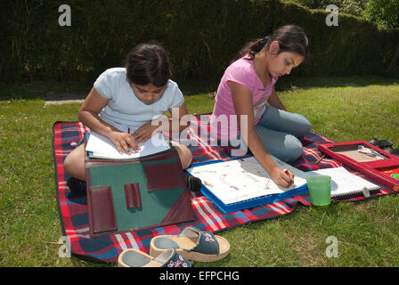 Se détendre au soleil deux jeunes filles s'amuser en faisant de l'artisanat et de l'écriture créative alors que sur une couverture de pique-nique Banque D'Images