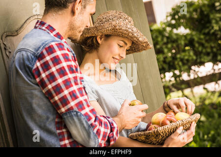 Couple leaning contre remise, young woman holding basket of apples Banque D'Images