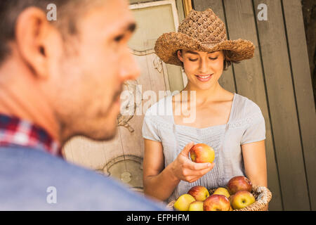 Young woman wearing straw hat, holding apple de panier, Mid adult man in foregound Banque D'Images