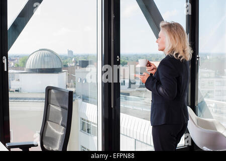 Businesswoman drinking coffee par fenêtre Banque D'Images