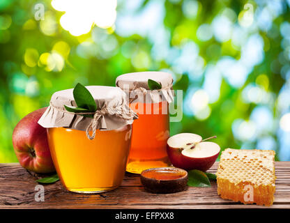 Les canettes en verre pleine de miel, pommes et peignes sur la vieille table en bois dans le jardin. Banque D'Images