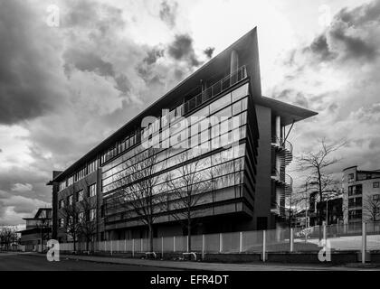 Photo en noir et blanc de l'immeuble de bureaux moderne avec ciel dramatique derrière. Bâtiment protégé par une clôture métallique et façade par une route Banque D'Images