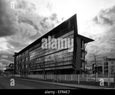 Photo en noir et blanc de l'immeuble de bureaux moderne avec ciel dramatique derrière. bâtir protégée par clôture métallique et façade par une route Banque D'Images