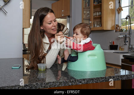 Mère nourrir bébé fille sur le comptoir de la cuisine Banque D'Images