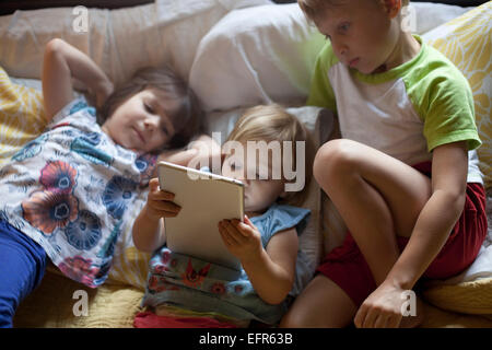 Trois jeunes enfants détente sur bed using digital tablet Banque D'Images