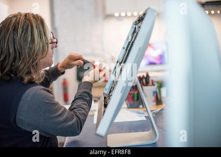 Atelier de réparation d'ordinateur. Un homme travaillant sur un écran d'ordinateur, à la réparer. Banque D'Images