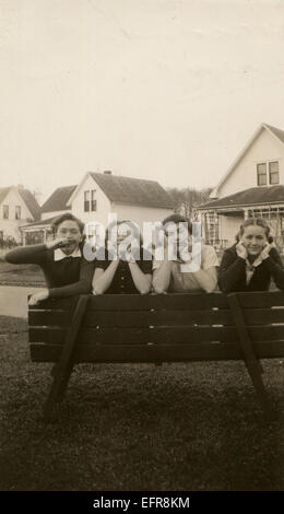 Le Canada. Dec 12, 2014. CIRCA 1950 : Reproduction d'une ancienne photo montre quatre filles avec des grimaces, posant sur un banc de bois sur le fond de la rue avec des maisons à deux étages © Igor Golovniov/ZUMA/ZUMAPRESS.com/Alamy fil Live News Banque D'Images