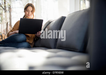 Femme assise sur un canapé en regardant son portable en souriant. Banque D'Images