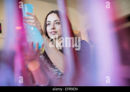 Femme tenant un vase de verre bleu. Vases rouges et roses au premier plan. Banque D'Images