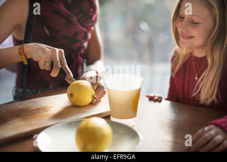 Une femme et une jeune fille souriante assis à une table, woman slicing un citron en deux. Banque D'Images