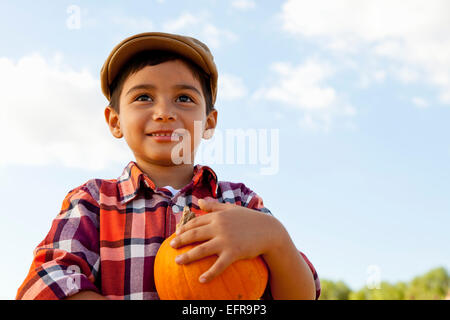 Portrait of boy holding pumpkin dans champ de citrouille Banque D'Images