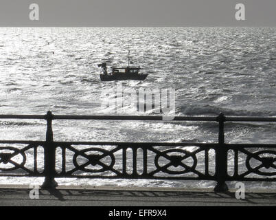 Un bateau de pêche les luttes contre une marée d'ouest au large de Brighton à la lumière du soleil tôt le matin dans la mer scintillante. Banque D'Images