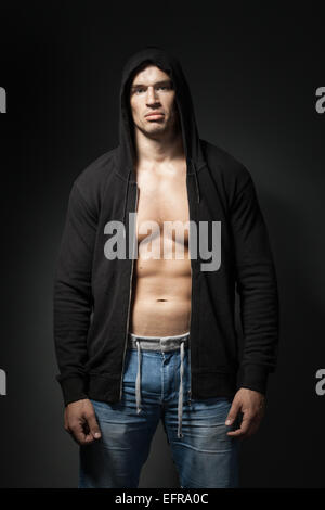 Strong man wearing hoodie noir isolé sur fond sombre Banque D'Images