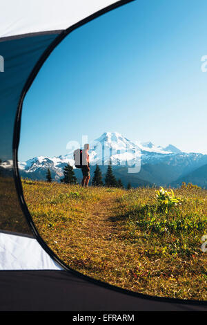Vue depuis l'intérieur d'une tente de camping d'un homme hiking across national forest land avec le mont Baker dans la distance. Banque D'Images