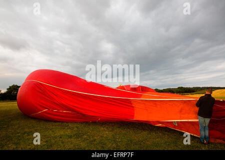 Aéronaute mâle rouge gonflage montgolfière en champ, south Oxfordshire, Angleterre Banque D'Images