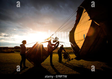 Le gonflage de l'équipage d'accueil hot air balloon at sunset, south Oxfordshire, Angleterre Banque D'Images